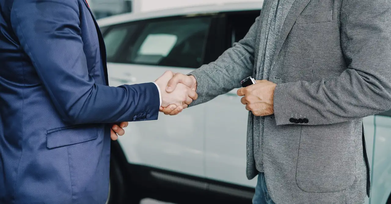 Two businessmen shaking hands in a car dealership, sealing a deal