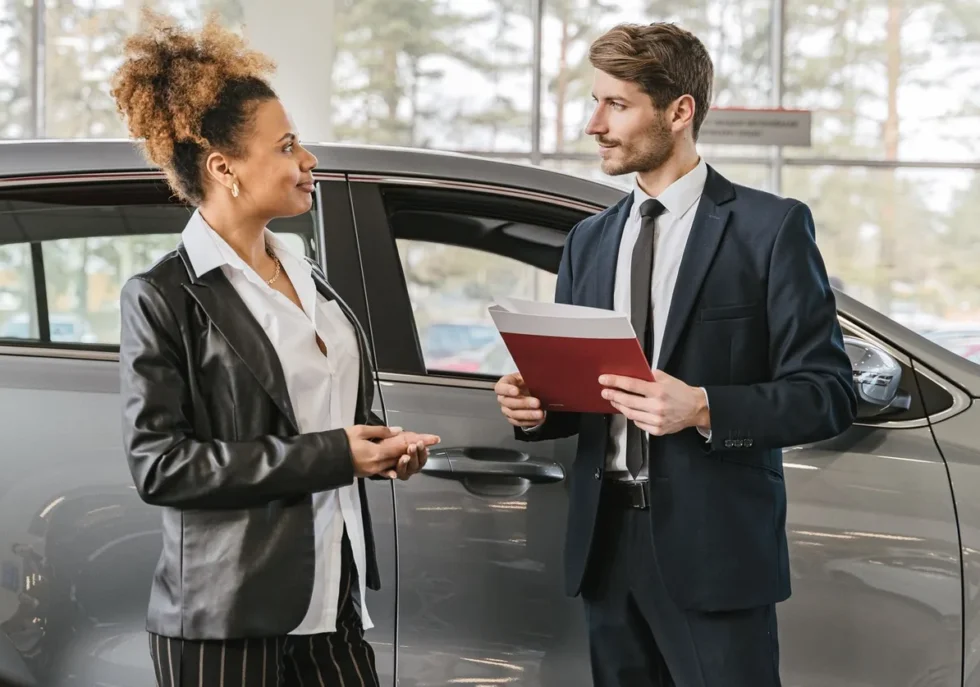 A woman discussing car purchase with a dealer inside a car dealership showroom