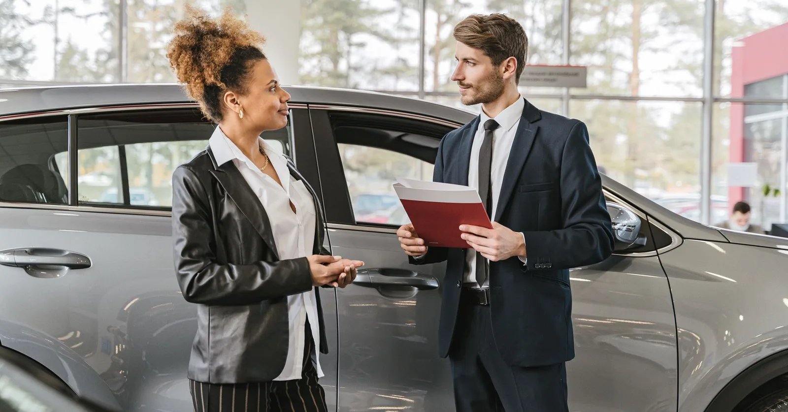 A woman discussing car purchase with a dealer inside a car dealership showroom